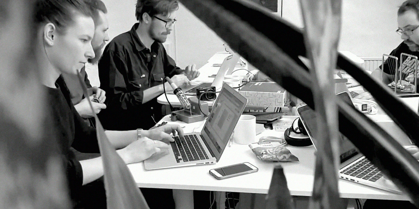 Hackers working side by side at laptops on a long table.