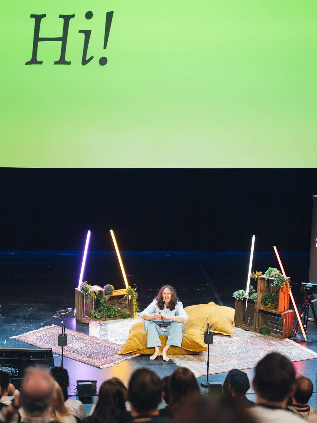 A host on a beanbag on stage, greeting the room from a big green Hi! slide