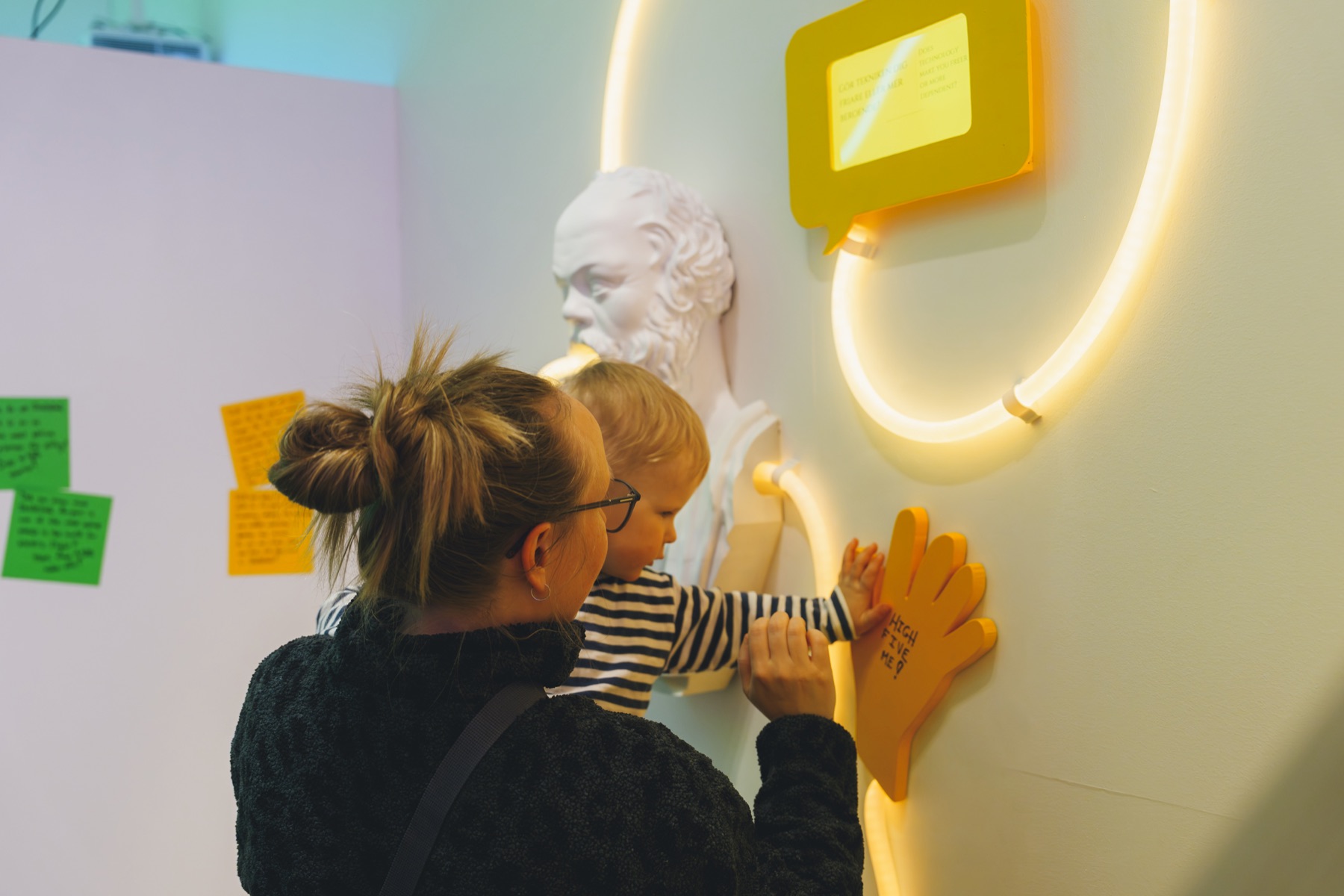 A parent and child high-fiving a yellow hand on the wall under a speech bubble