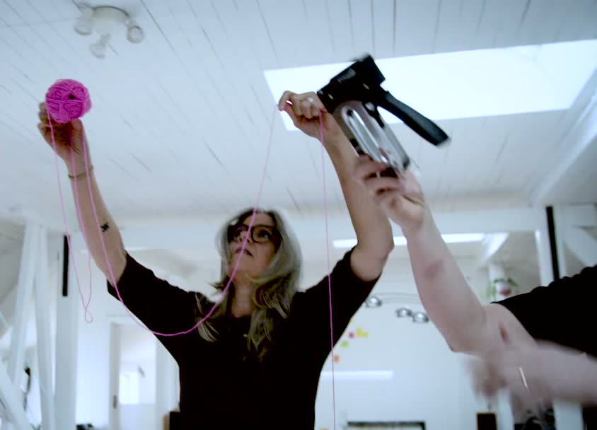 A participant stapling yarn up toward the ceiling